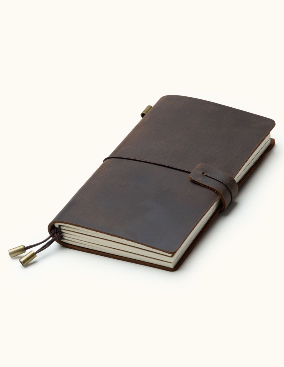 Handcrafted coffee brown leather travel journal with elastic closure, refillable notebook inserts, and brass charms, perfect for travel notes, sketching, and journaling.