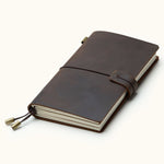 Handcrafted coffee brown leather travel journal with elastic closure, refillable notebook inserts, and brass charms, perfect for travel notes, sketching, and journaling.
