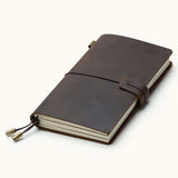 Handcrafted coffee brown leather travel journal with elastic closure, refillable notebook inserts, and brass charms, perfect for travel notes, sketching, and journaling.