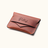Handcrafted brown leather wallet with personalized name engraving, shown in angled view highlighting the slim minimalist card holder and envelope flap design.