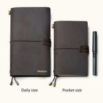 Two handmade coffee brown leather travel notebooks in daily and pocket sizes with elastic closure and custom name engraving, shown with a pen for size reference.