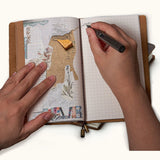 Person writing in a handmade leather travel journal with a grid refill while using the notebook for collage scrapbooking and journaling.