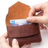Person inserting a credit card into a handcrafted brown leather wallet with personalized name engraving, showing the slim minimalist card holder in use.