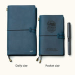 Two handmade navy blue leather travel notebooks in daily and pocket sizes with elastic closure, custom engraving, and refillable design, shown with pen for size reference.