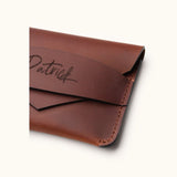 Close-up of a handcrafted brown leather wallet showing fine stitching, envelope flap design, and personalized name engraving on the slim minimalist card holder.