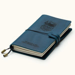 Handcrafted navy blue leather travel journal with elastic closure, custom engraved mountain adventure design, refillable pages, and brass charms, perfect for travel notes and journaling.