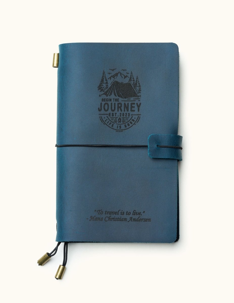 Front view of a handcrafted navy blue leather travel journal with custom engraved mountain adventure design and inspirational quote, elastic closure, and brass charms, refillable for travel notes.