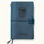 Front view of a handcrafted navy blue leather travel journal with custom engraved mountain adventure design and inspirational quote, elastic closure, and brass charms, refillable for travel notes.
