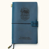 Front view of a handcrafted navy blue leather travel journal with custom engraved mountain adventure design and inspirational quote, elastic closure, and brass charms, refillable for travel notes.