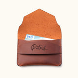 Handcrafted brown leather wallet shown open with visible suede interior, holding a credit card in the personalized slim card holder with name engraving and envelope flap design.