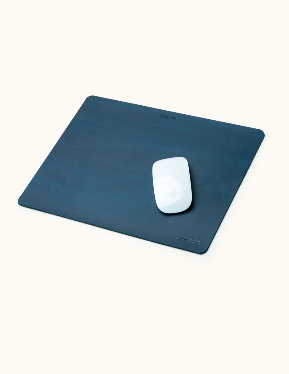 Blue personalized leather mouse pad with engraved name, shown with Apple Magic Mouse on top