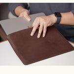 Person inserting a MacBook into a customizable coffee color full-grain leather sleeve, shown in real-life use