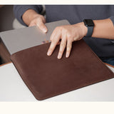 Person inserting a MacBook into a customizable coffee color full-grain leather sleeve, shown in real-life use