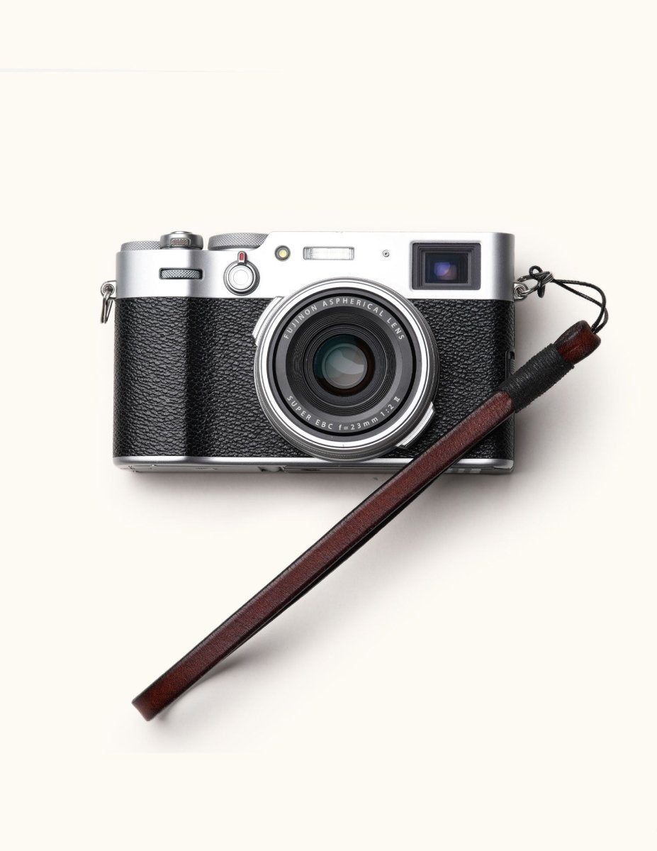 Slim full-grain leather camera wrist strap in coffee color, attached to a Fujifilm camera, highlighting its elegant and secure fit for everyday photography