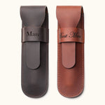 Two personalized leather single cigar cases in dark brown and tan, engraved with names and titles such as "Marc" and "Best Man", featuring a flap closure and stitched edges