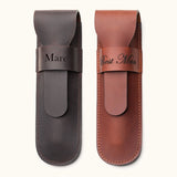 Two personalized leather single cigar cases in dark brown and tan, engraved with names and titles such as "Marc" and "Best Man", featuring a flap closure and stitched edges