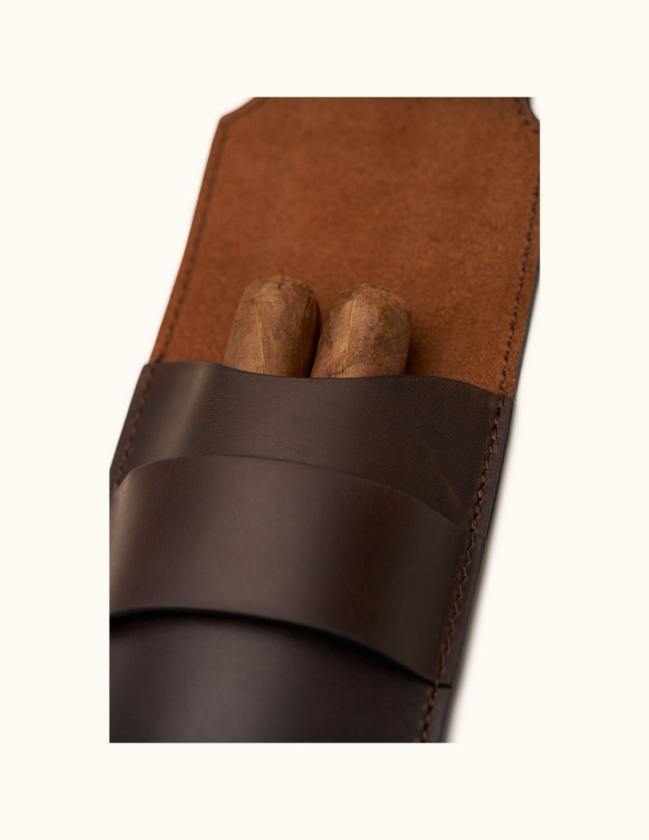 Close-up of a dark brown leather double cigar case holding two cigars, showing the suede-lined interior and precision hand-stitching