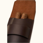 Close-up of a dark brown leather double cigar case holding two cigars, showing the suede-lined interior and precision hand-stitching