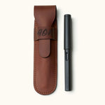 Personalized leather fountain pen case with engraved initials, shown next to a black LAMY pen. Crafted from full-grain leather with flap closure and fine stitching