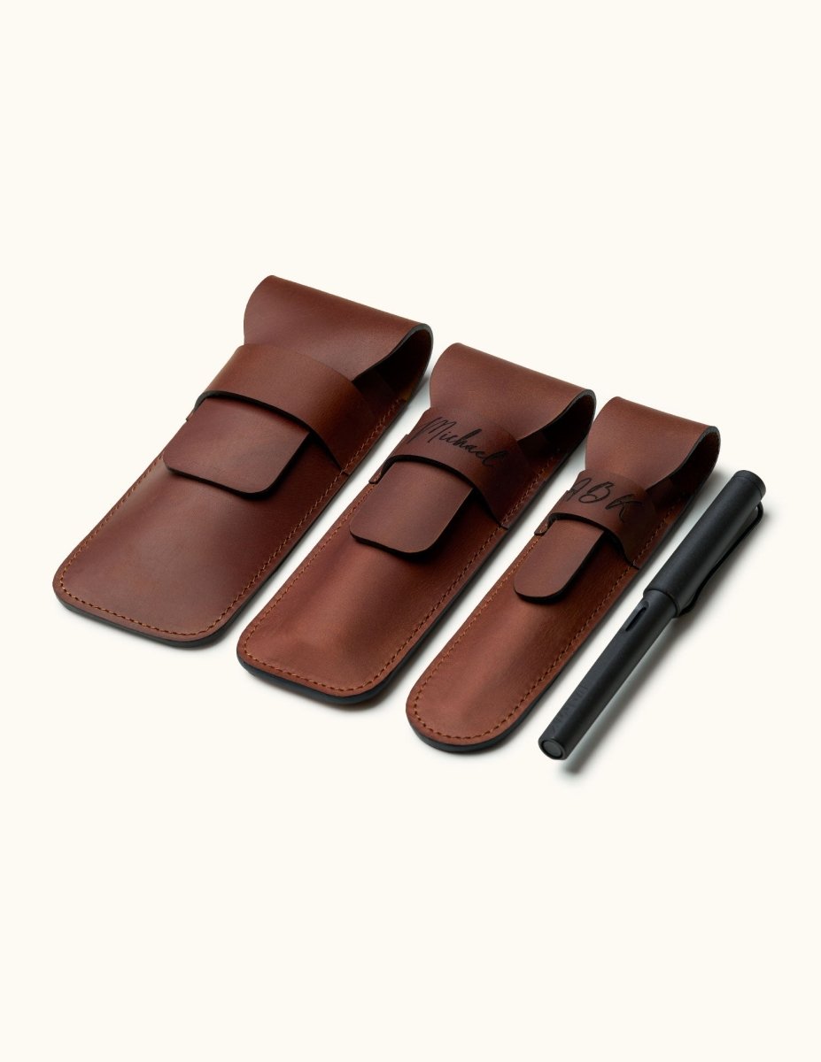 Three sizes of handmade full-grain leather pen cases for 1, 2, or 3 pens, shown with a black LAMY fountain pen for scale. Personalized engraving available