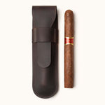 Handmade dark brown leather cigar pouch designed for one cigar, shown with a full-sized cigar beside it. A minimalist, travel-friendly accessory for cigar lovers
