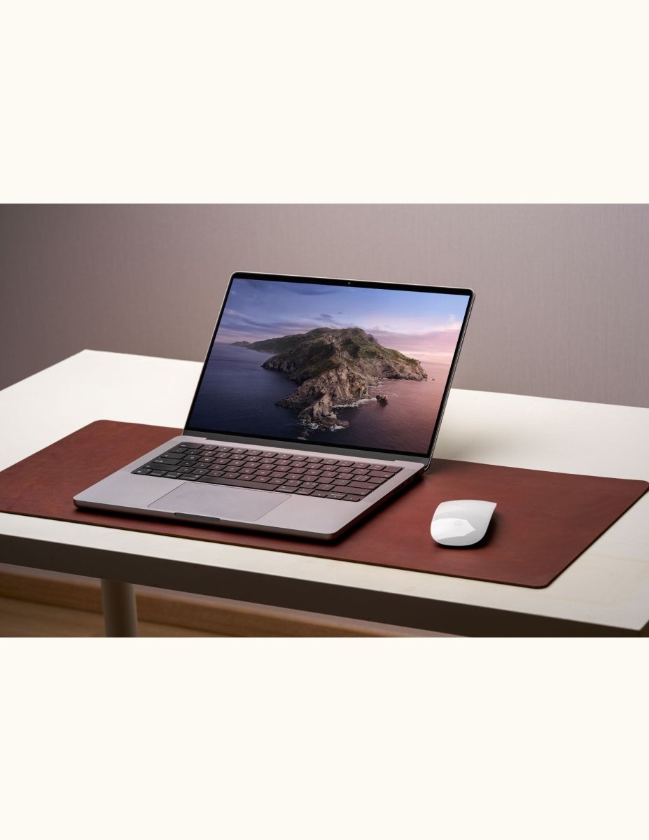 Office setup with leather desk pad, laptop, and Magic Mouse on white table – large mouse pad used as workspace mat