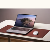Office setup with leather desk pad, laptop, and Magic Mouse on white table – large mouse pad used as workspace mat
