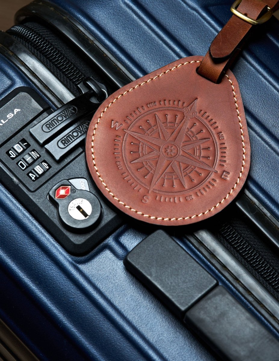 Brown leather luggage tag with compass design attached to a blue suitcase, showing real travel use