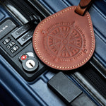 Brown leather luggage tag with compass design attached to a blue suitcase, showing real travel use