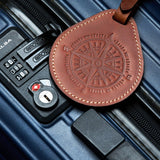 Brown leather luggage tag with compass design attached to a blue suitcase, showing real travel use