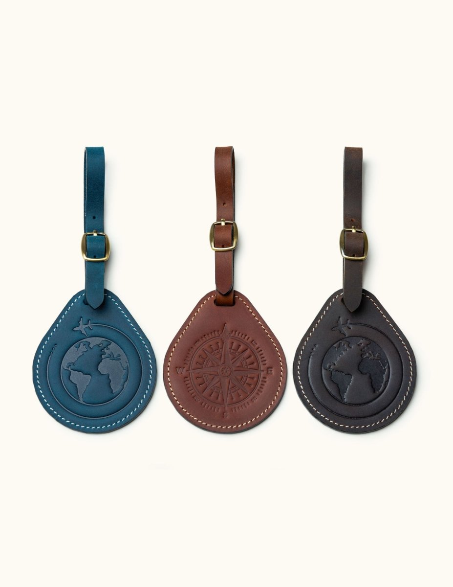 Set of three round leather luggage tags in navy, brown, and black with engraved globe and compass designs