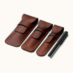 Three personalized leather pen cases in different sizes displayed next to a black fountain pen, showing engraving options and flap closure style