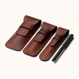 Three personalized leather pen cases in different sizes displayed next to a black fountain pen, showing engraving options and flap closure style