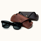 Brown and dark brown handcrafted leather sunglasses cases displayed with black sunglasses, personalized with initials