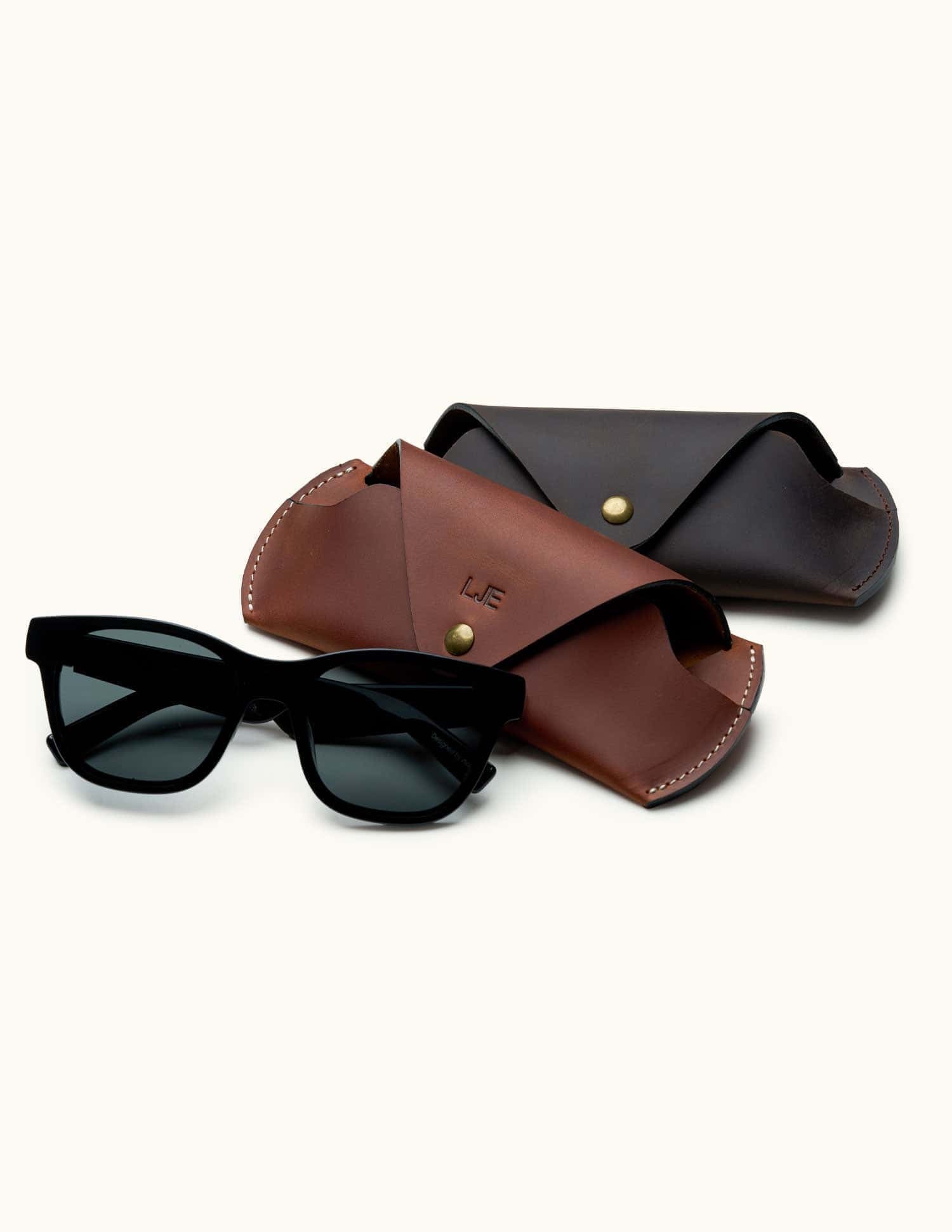 Brown and dark brown handcrafted leather sunglasses cases displayed with black sunglasses, personalized with initials