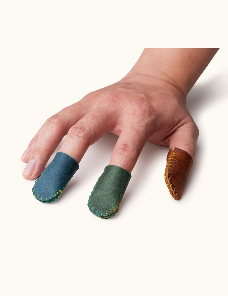 Hand wearing blue, green, and brown leather thimbles, showing fit for sewing or crafting.