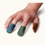 Hand wearing blue, green, and brown leather thimbles, showing fit for sewing or crafting.