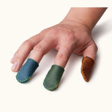 Hand wearing blue, green, and brown leather thimbles, showing fit for sewing or crafting.