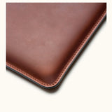 Close-up of corner stitching on vintage brown full-grain leather MacBook Pro sleeve, showing craftsmanship and texture