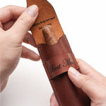 Hands placing a cigar into a personalized leather case engraved with "Best Man" on the outside and "Will you be my best man?" on the inner flap. A sentimental groomsman proposal gift idea