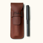 Handmade full-grain leather pen case designed for two pens, shown with a black LAMY fountain pen. Personalized with name engraving and secure flap closure