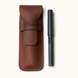 Handmade full-grain leather pen case designed for two pens, shown with a black LAMY fountain pen. Personalized with name engraving and secure flap closure