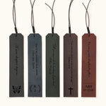 Five personalized leather bookmarks in different colors, each engraved with custom quotes, initials, or dates, with decorative tassel cords on top