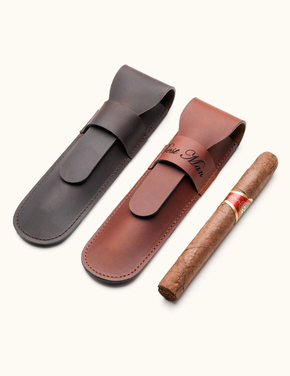 Two personalized leather cigar cases in dark brown and chestnut, one engraved with "Best Man", shown next to a single cigar. A stylish gift idea for groomsmen or cigar lovers