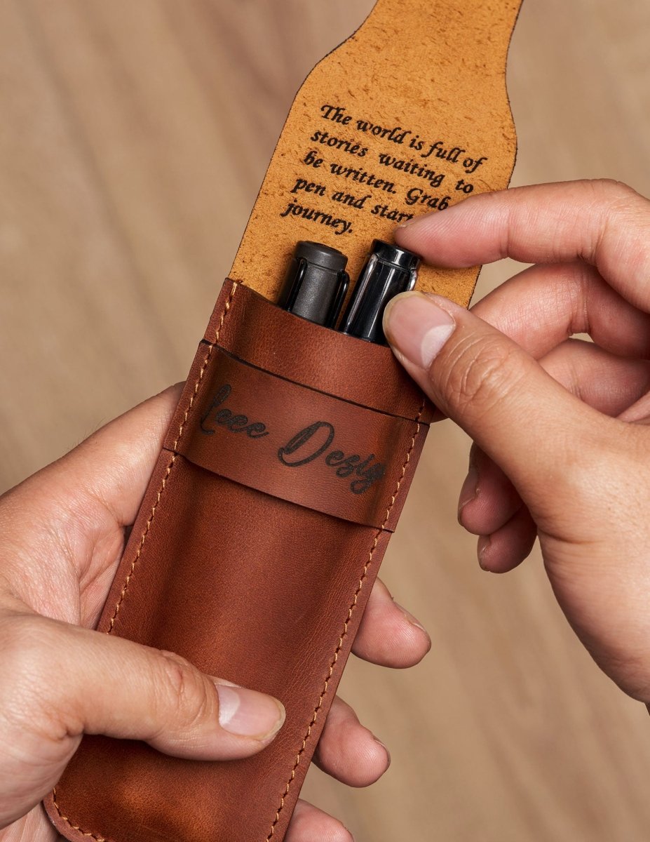 Hands holding a personalized full-grain leather pen case with two pens inside and an engraved inspirational message under the flap