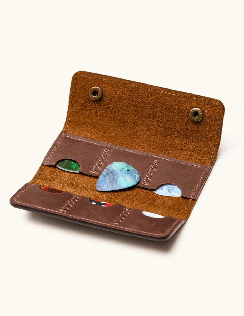 Open view of handcrafted leather guitar pick holder with six slots, showing colorful guitar picks and suede interior