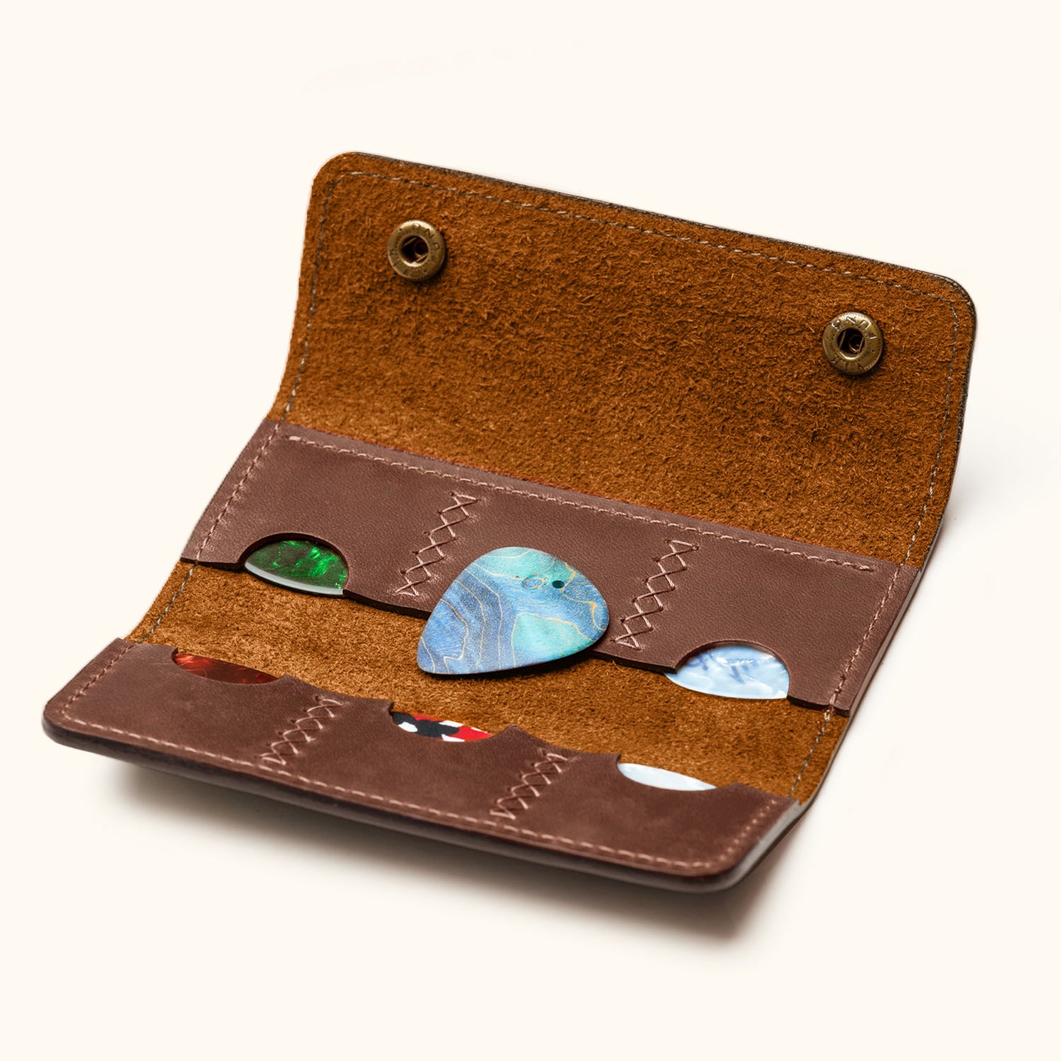 Open view of handcrafted leather guitar pick holder with six slots, showing colorful guitar picks and suede interior