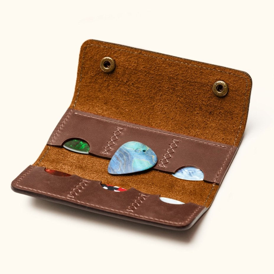 Open view of handcrafted leather guitar pick holder with six slots, showing colorful guitar picks and suede interior