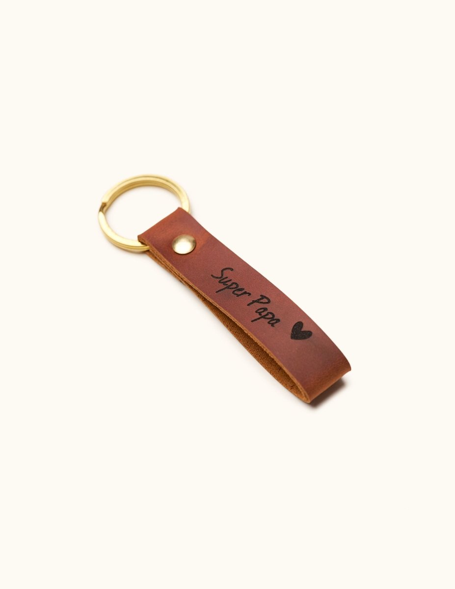 Handmade brown leather keychain with gold keyring, engraved with “Super Papa” and a heart, shown angled, perfect personalized Father’s Day or dad birthday gift.