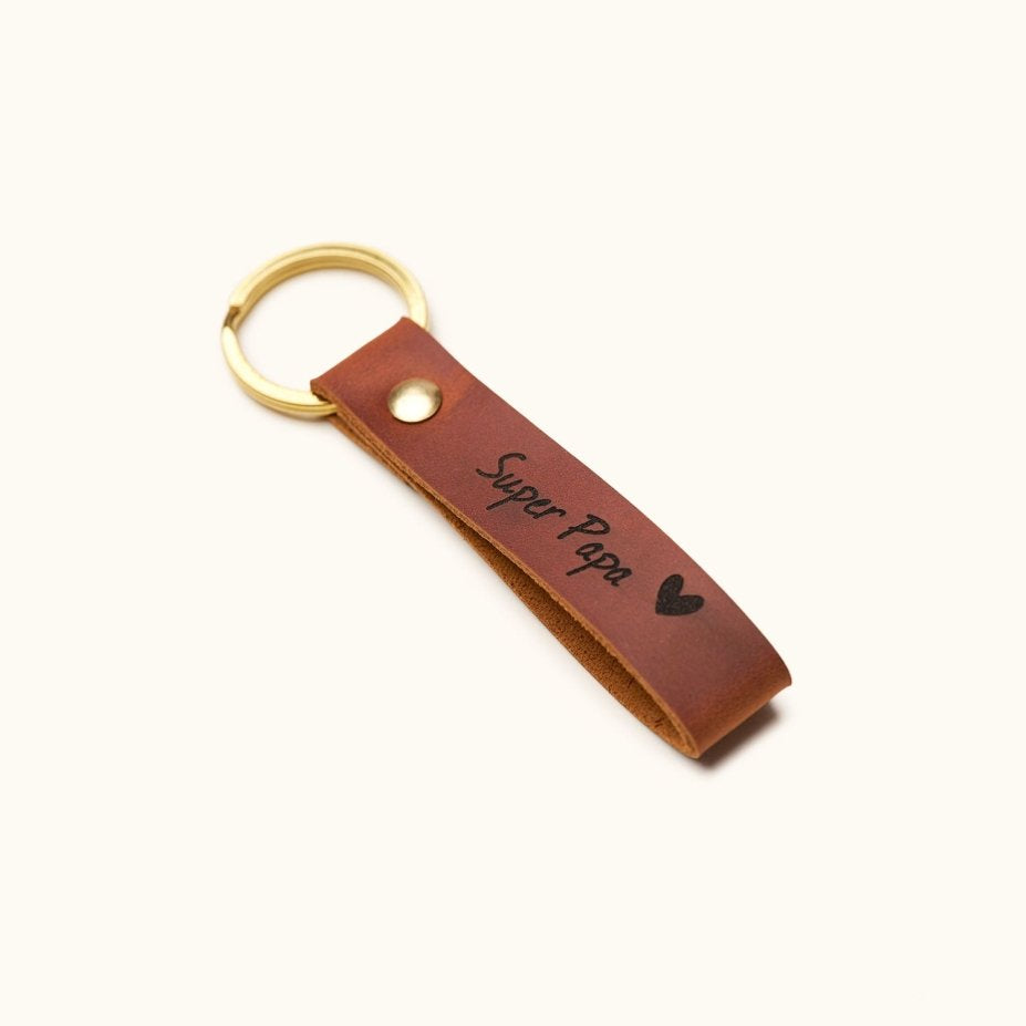 Handmade brown leather keychain with gold keyring, engraved with “Super Papa” and a heart, shown angled, perfect personalized Father’s Day or dad birthday gift.